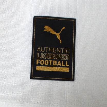 Offizielles Puma Borussia Mönchengladbach Heimtrikot der Saison 2025/26 für Kinder in traditionellem Weiß mit grünen und schwarzen Akzenten sowie eingesticktem Vereinswappen – Neu mit Etikett. Detailansicht Authentic Logo.