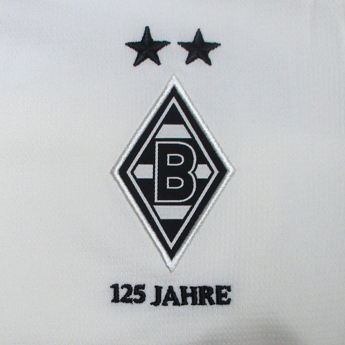 Offizielles Puma Borussia Mönchengladbach Heimtrikot der Saison 2025/26 für Kinder in traditionellem Weiß mit grünen und schwarzen Akzenten sowie eingesticktem Vereinswappen – Neu mit Etikett. Detailsansicht Raute.