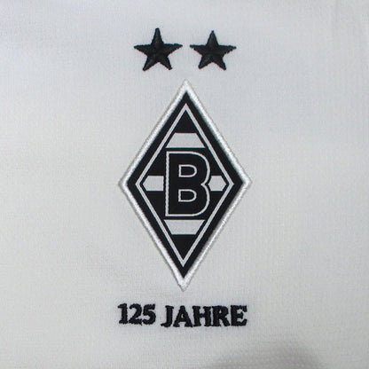 Offizielles Puma Borussia Mönchengladbach Heimtrikot der Saison 2025/26 für Kinder in traditionellem Weiß mit grünen und schwarzen Akzenten sowie eingesticktem Vereinswappen – Neu mit Etikett. Detailsansicht Raute.