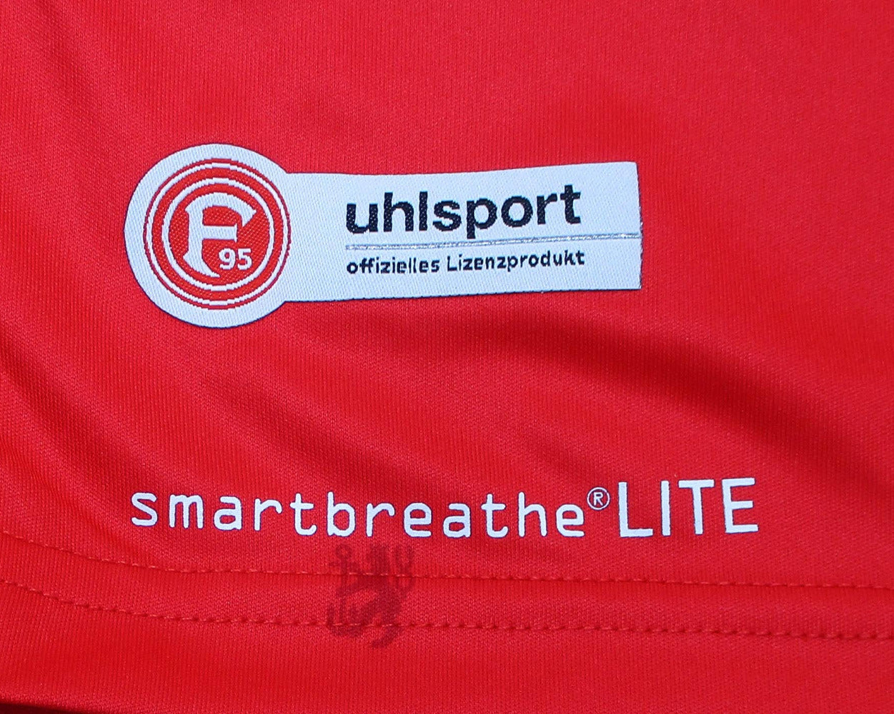 Rotes offizielles Fortuna Düsseldorf Heimtrikot 2020/21 von Uhlsport in Herrengröße. Detailansicht Saum.